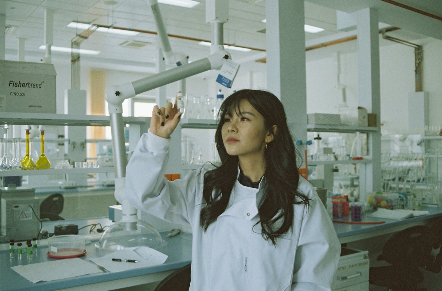 Young woman in lab coat examines vial in modern laboratory.